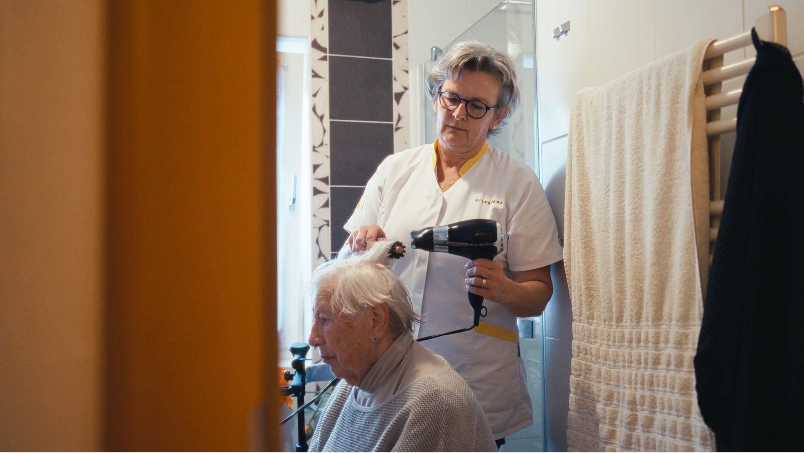 Eine Pflegerin föhnt einer älteren Dame die Haare